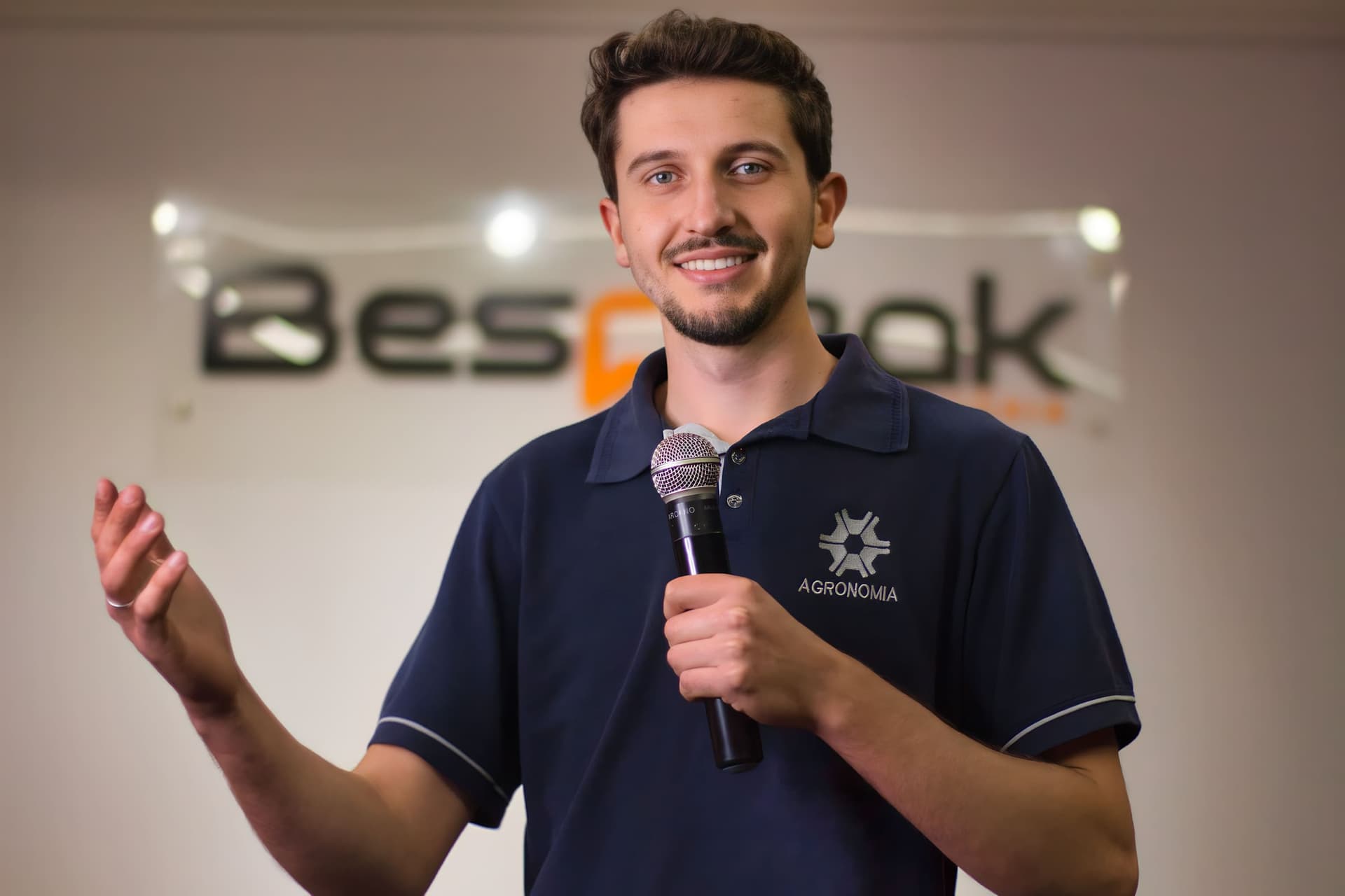 Aluno sorri e fala ao microfone diante do painel da Bespeak