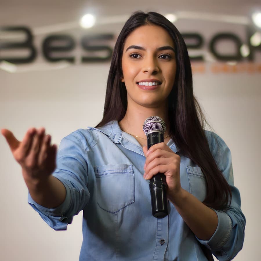 Aluna estende a mão para a turma enquanto fala ao microfone